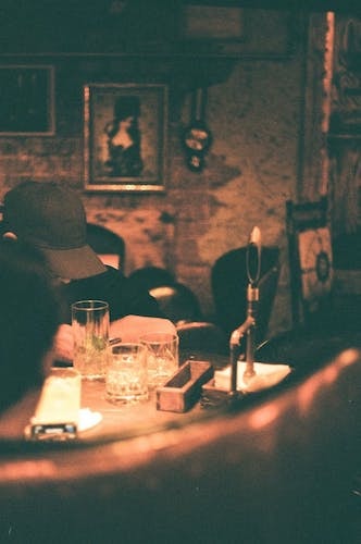 Man in a black cap enjoying a sit with a drink under the stairs at a local speakeasy bar