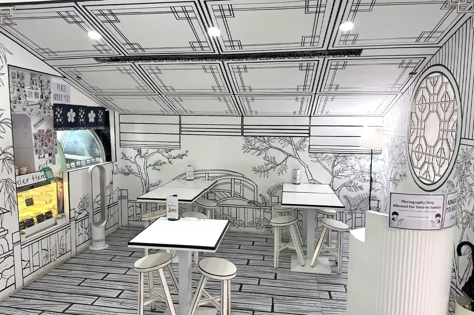 The interior of Cafe Monochrome in Singapore, featuring 2D hand-drawn line art on the walls and ceiling, white tables, and stools.
