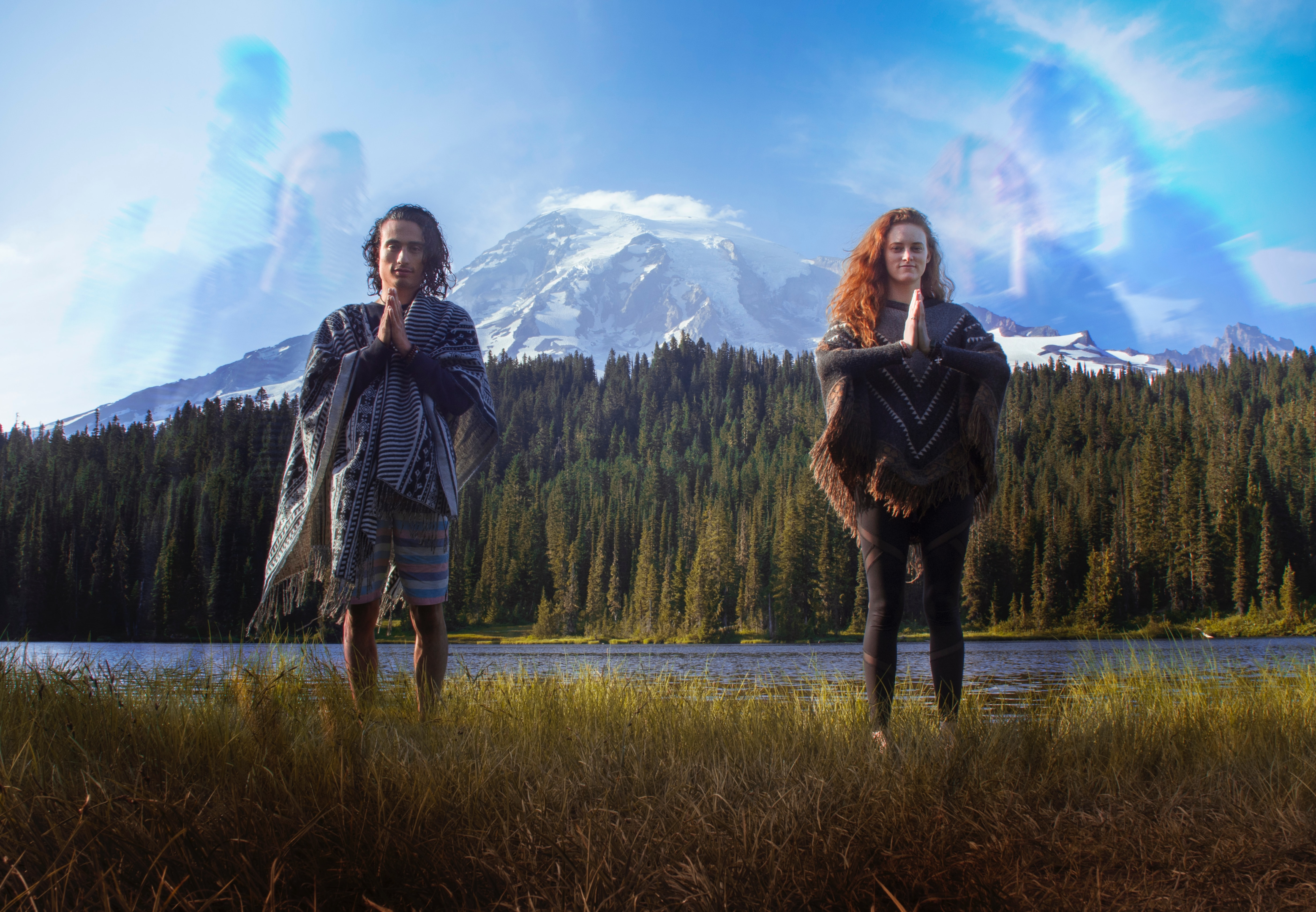 two people standing with prayer hands in front of a lake with a forest and mountain behind them