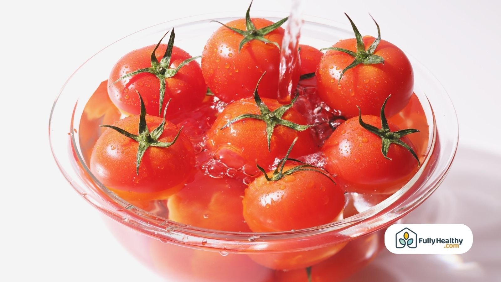 Cherry tomatoes being washed in a clear glass bowl with water