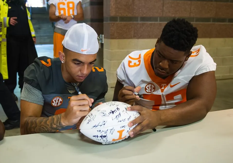 University of Tennessee football players signing autographed footballs during a fan event, highlighting NIL fan engagement opportunities.