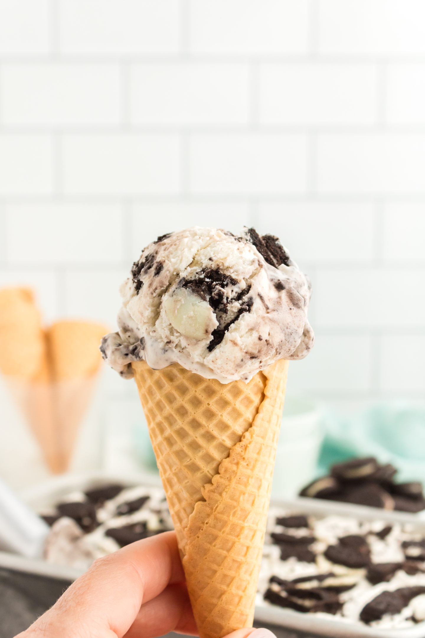 hand holding a waffle cone with a scoop of cookies and cream ice cream