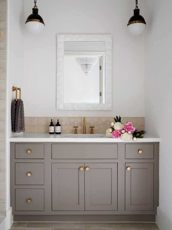 a feminine bathroom with brass detailing and a single vanity with scalloped tile