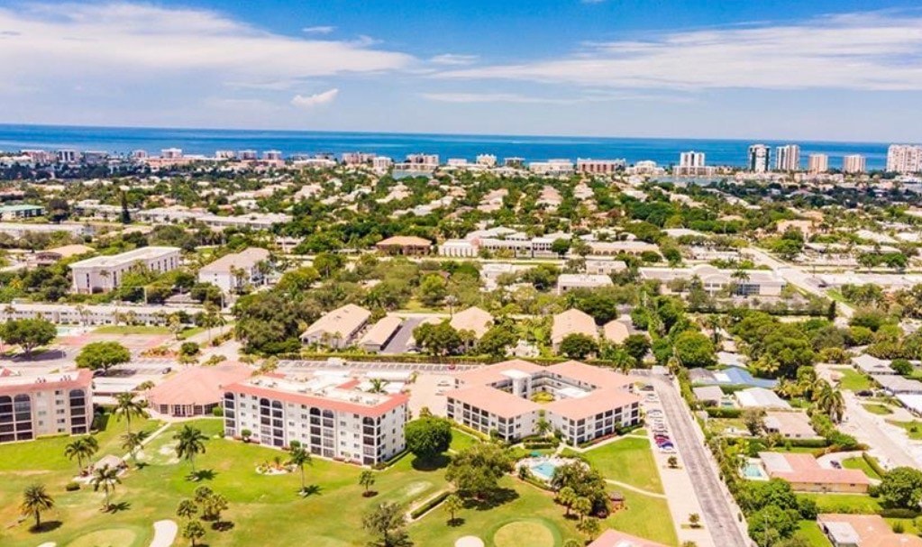 The image shows the tranquil High Point Country Club golf course bathed in the warm hues of a stunning Naples sunset, framed by swaying palm trees. This picturesque scene highlights the peaceful golf course vistas and serene ambiance that the community offers.