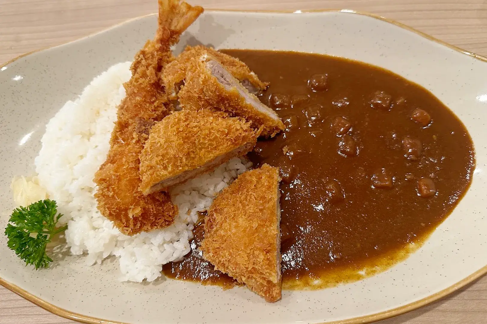 A Japanese curry platter from Gochi So Sokudo in Singapore, featuring deep-fried pork katsu and a large shrimp tempura served with savory curry sauce and rice.
