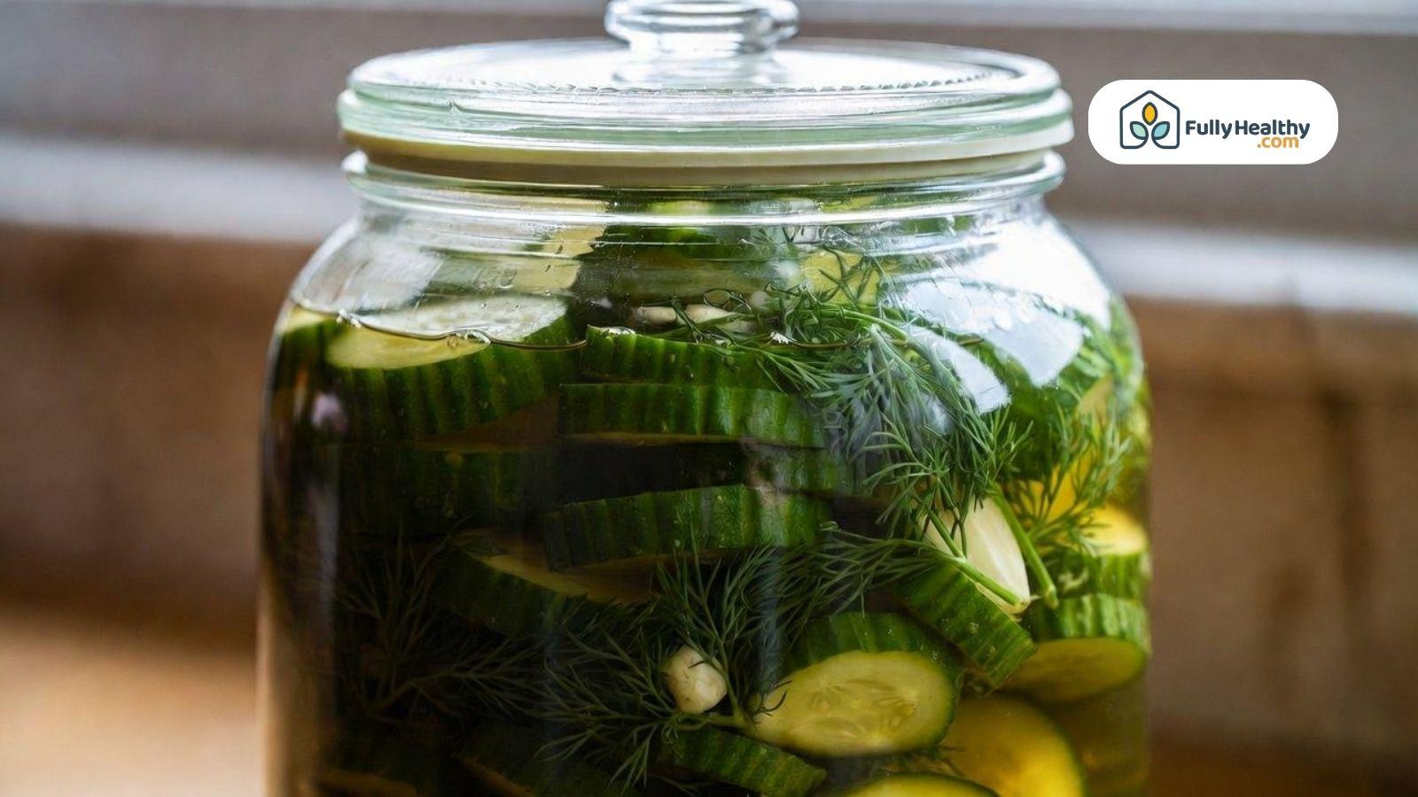 Glass jar filled with cucumber slices in vinegar brine with dill and garlic