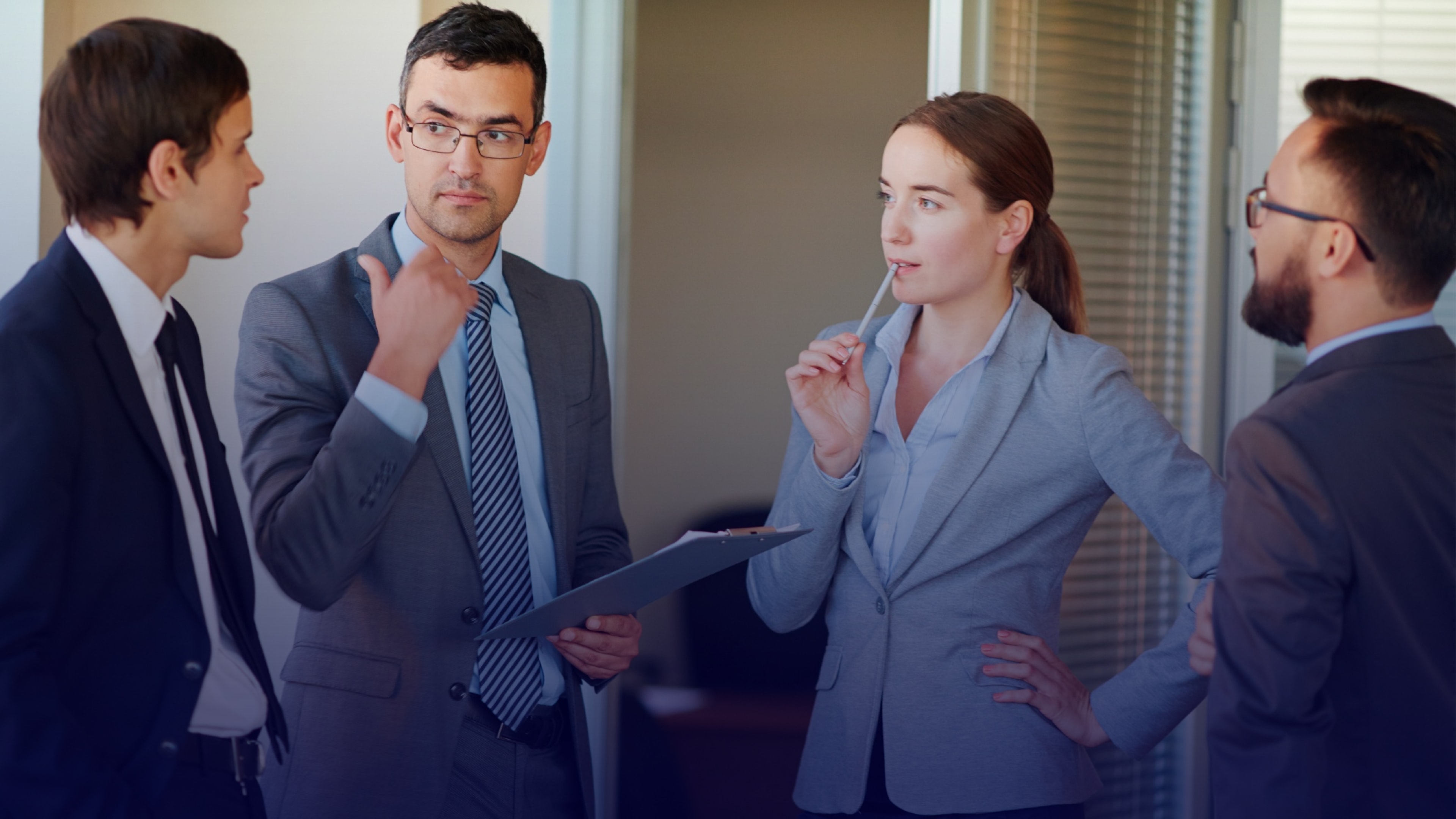 Team in business attire having a discussion in an office hallway, representing collaboration on critical communications, safety measures, and business continuity planning.