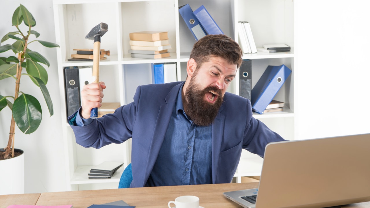 smashing laptop with hammer, frustrated man