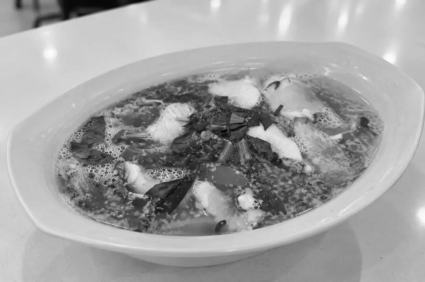 A bowl of Red Grouper Fish Head Soup with chunky fish pieces, tofu, vegetables, and a rich milky broth.