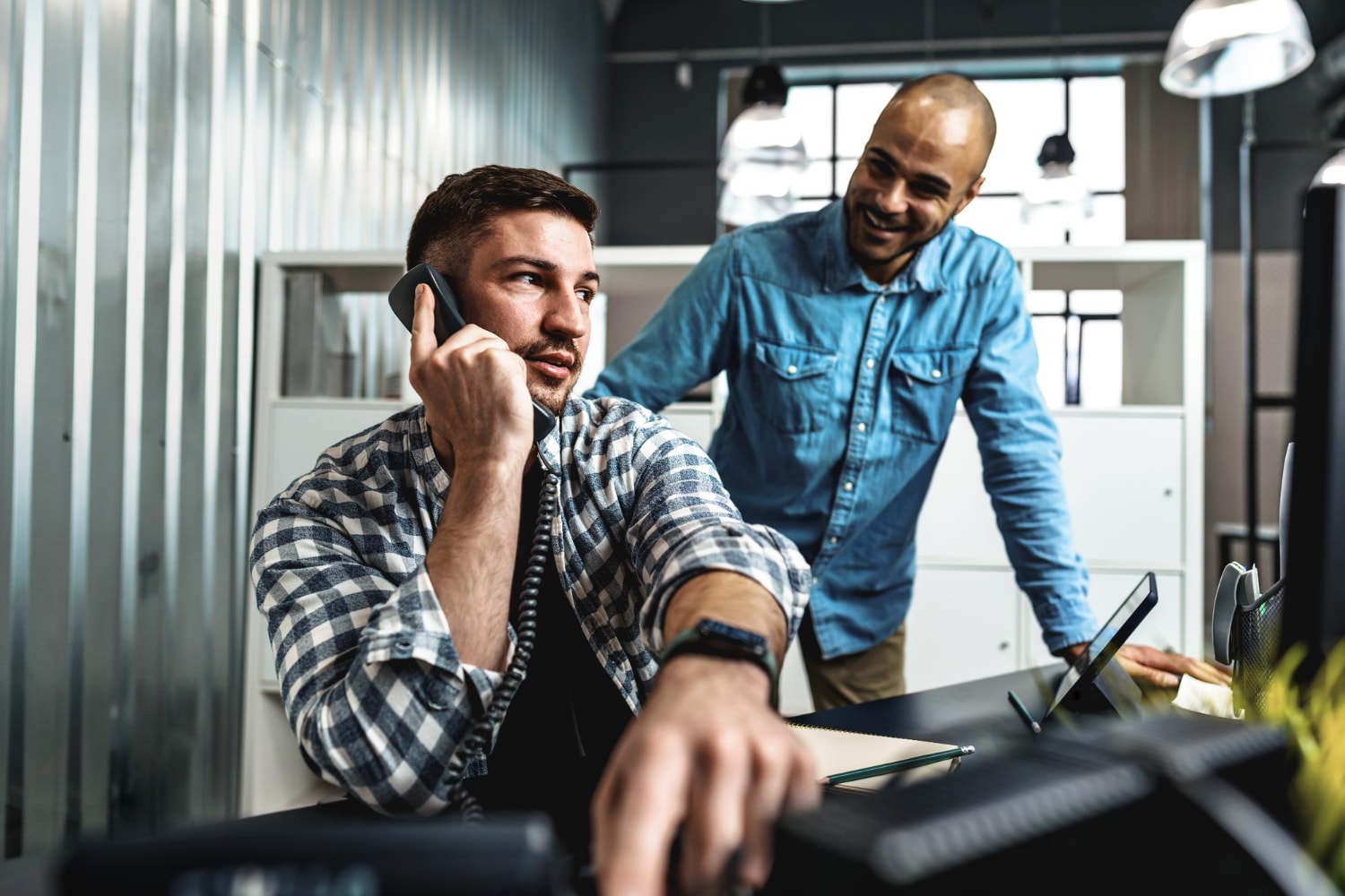 Coworkers engage in a conversation using simple business phone systems in a modern office, showcasing affordable and streamlined communication solutions for business teams.