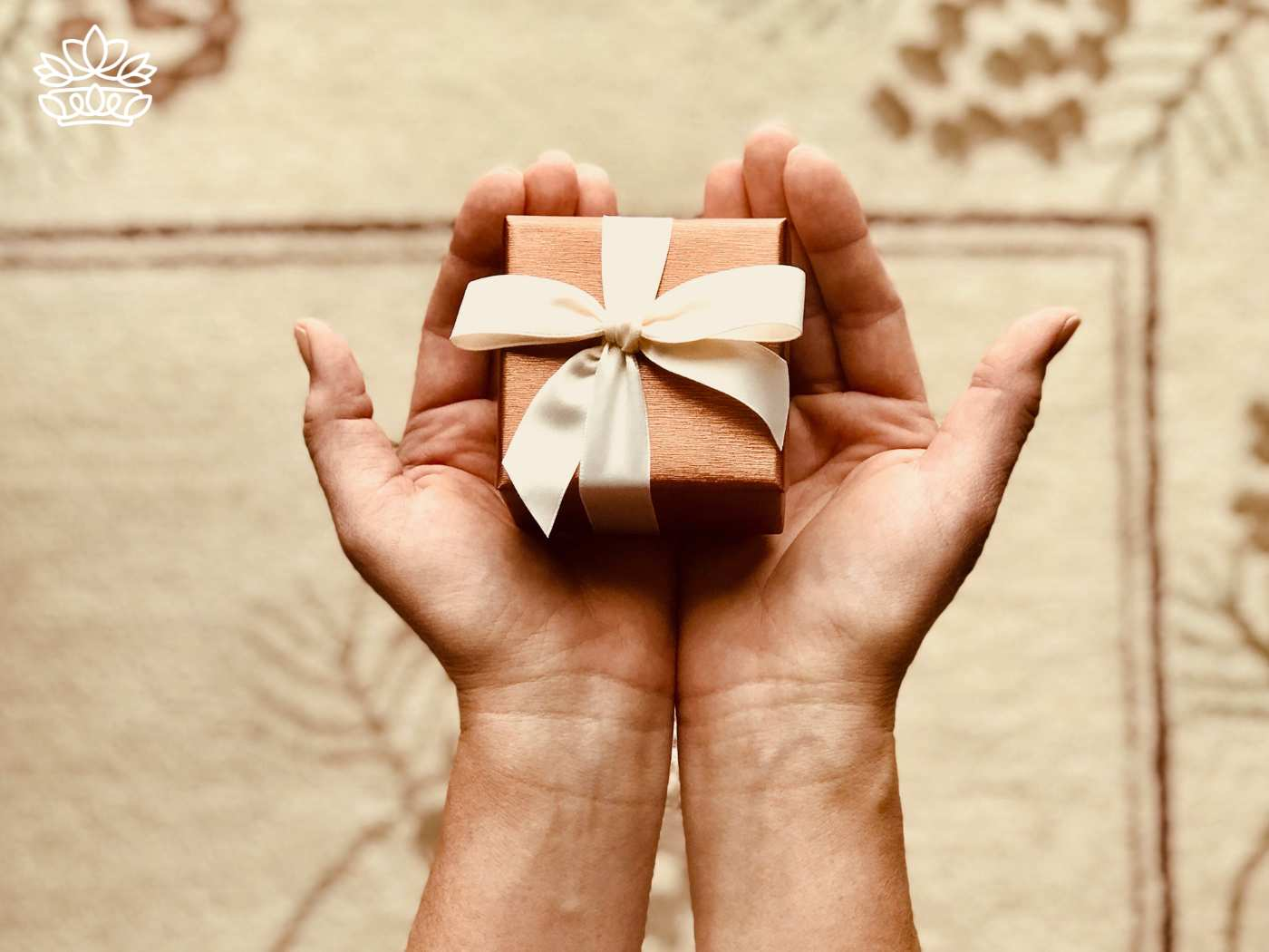A pair of hands holding a small gift box with a white ribbon, showcasing the perfect gift from the Gift Boxes for Her Collection - South Africa's excellent service in hampers for ladies - Fabulous Flowers and Gifts