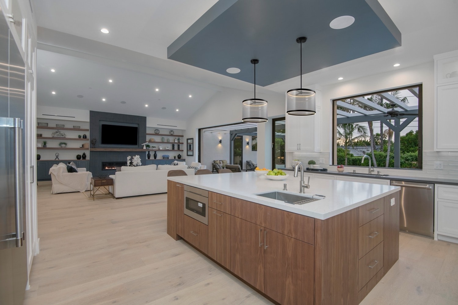 Contemporary kitchen with Artcraft Lighting Cora pendant lights over a spacious island, featuring wood cabinetry, white countertops, and an open living area.