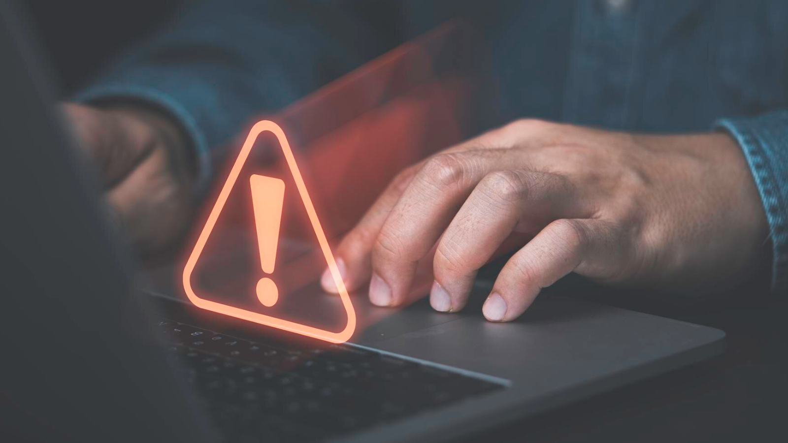 Hands typing near a glowing warning icon, illustrating how not implementing a better management strategy can reduce growth effectiveness and handling of sensitive data.