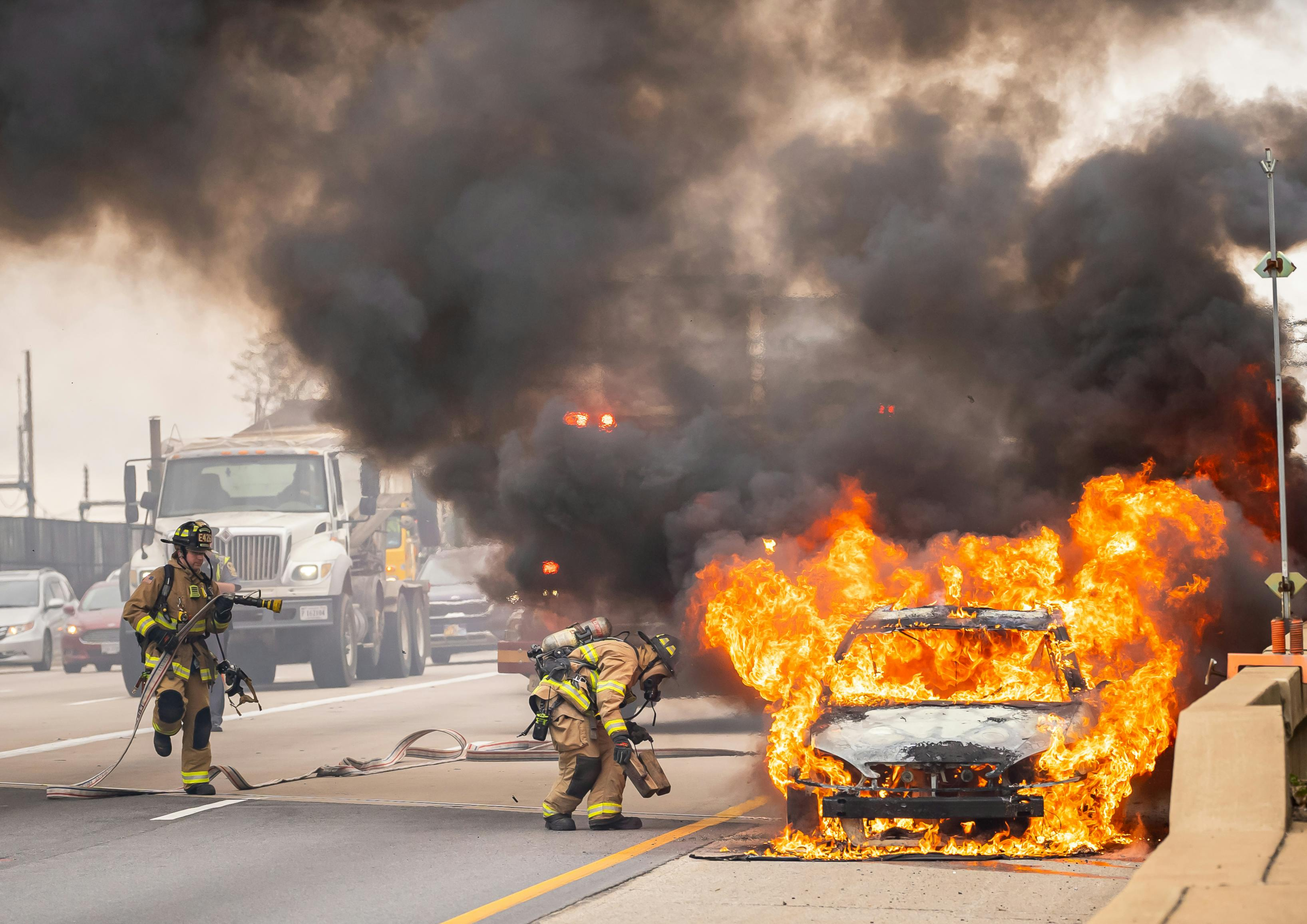 Two firefighters extinguishing a vehicle on fire on the highway.