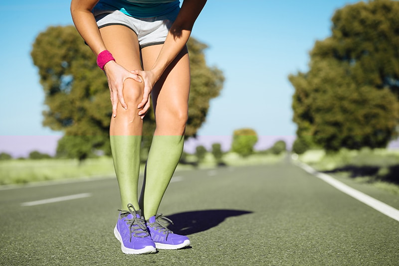 Runner on a road holding a sore knee, representing physical therapy techniques for knee pain from overuse and training.