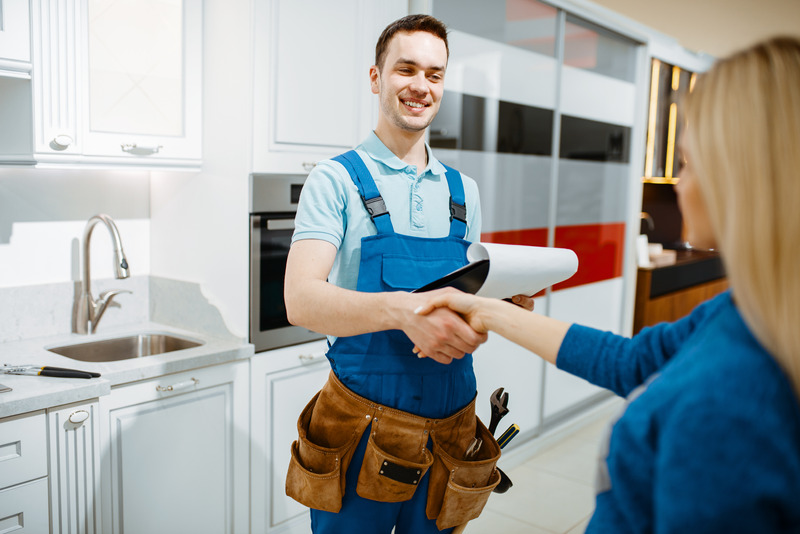 Installateur im Blaumann reicht einer Kundin in der Küche Unterlagen.