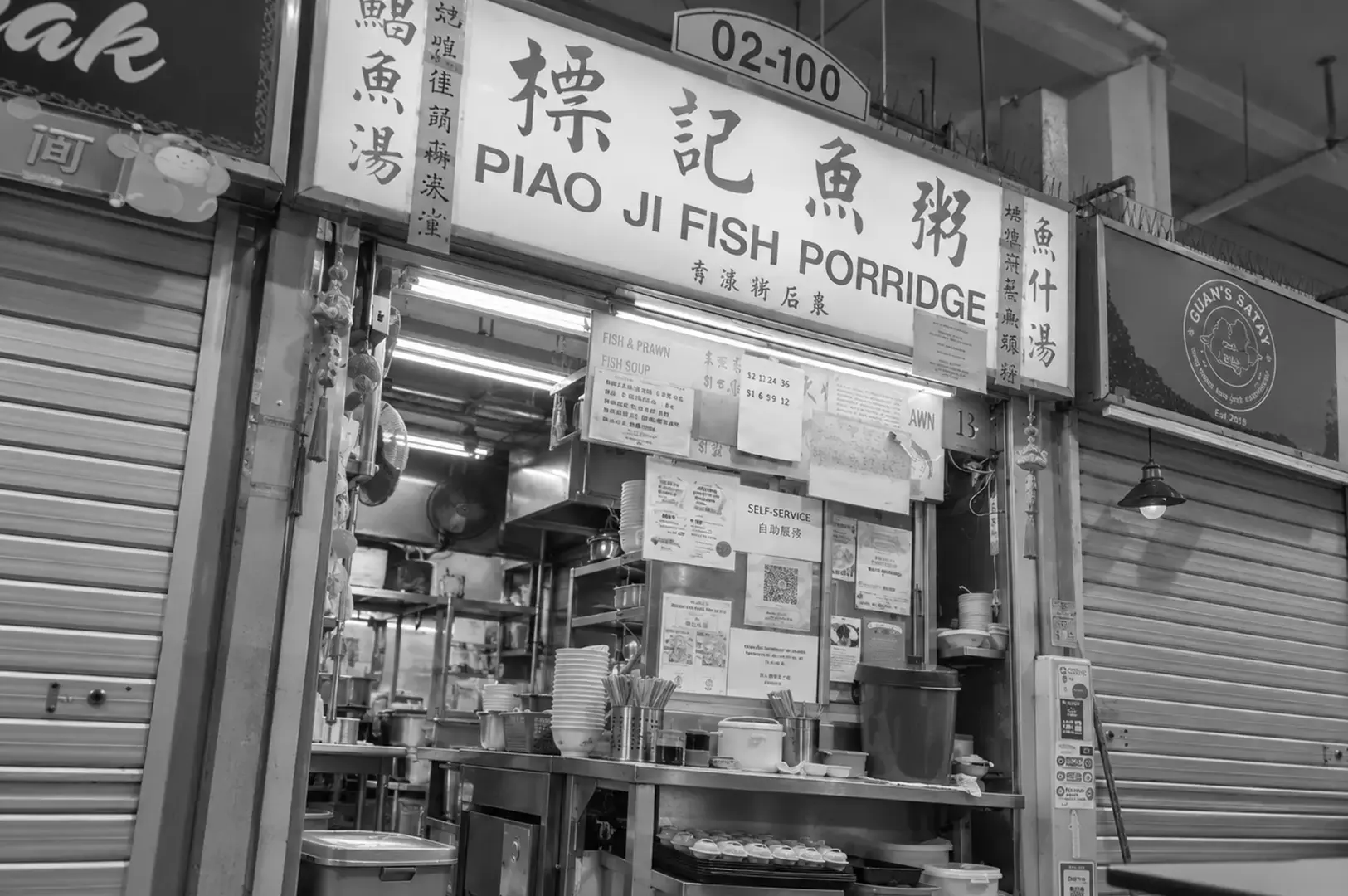 A local fish soup stall with illuminated menu boards, cooking equipment, bowls, and a busy open preparation counter.