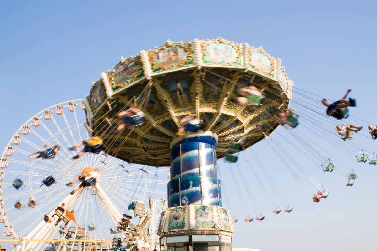 Colorful swing ride spinning at the Wildwood Boardwalk with the Ferris wheel in the background on a clear summer day.