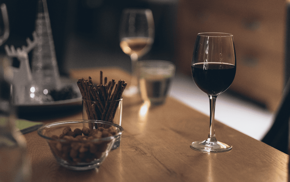 Een glas rode en witte wijn op een tafel waar ook borrelhapjes op staan.
