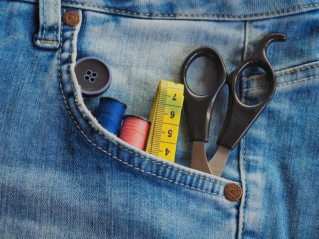 image of a denim pocket holding a button, thread, scissors, and measureing tape to alter fabric in a shop for garments and clothing