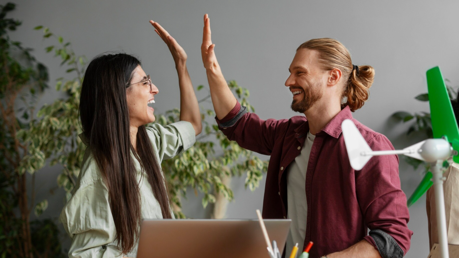 Smiling coworkers giving a high five near a laptop, celebrating the difference dedicated Internet access makes when it comes to capabilities and peace of mind.