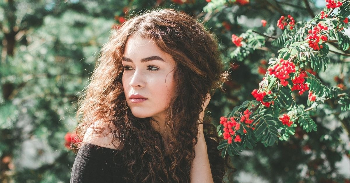 Creator thinking about her tax plan while posing near red berries, wearing a black top outdoors.