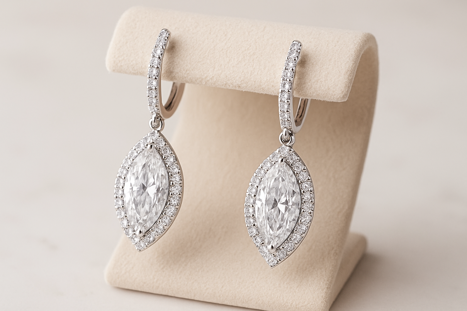 Marquise formos deimantų auskarai su halo dizainu, įstatyti į balto aukso pagrindą, eksponuojami ant šviesiai smėlinio papuošalų stovo.