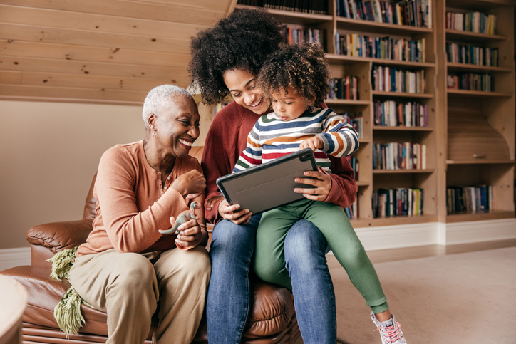 Grandmother, her adult daughter, and grandson looking at something on a tablet.