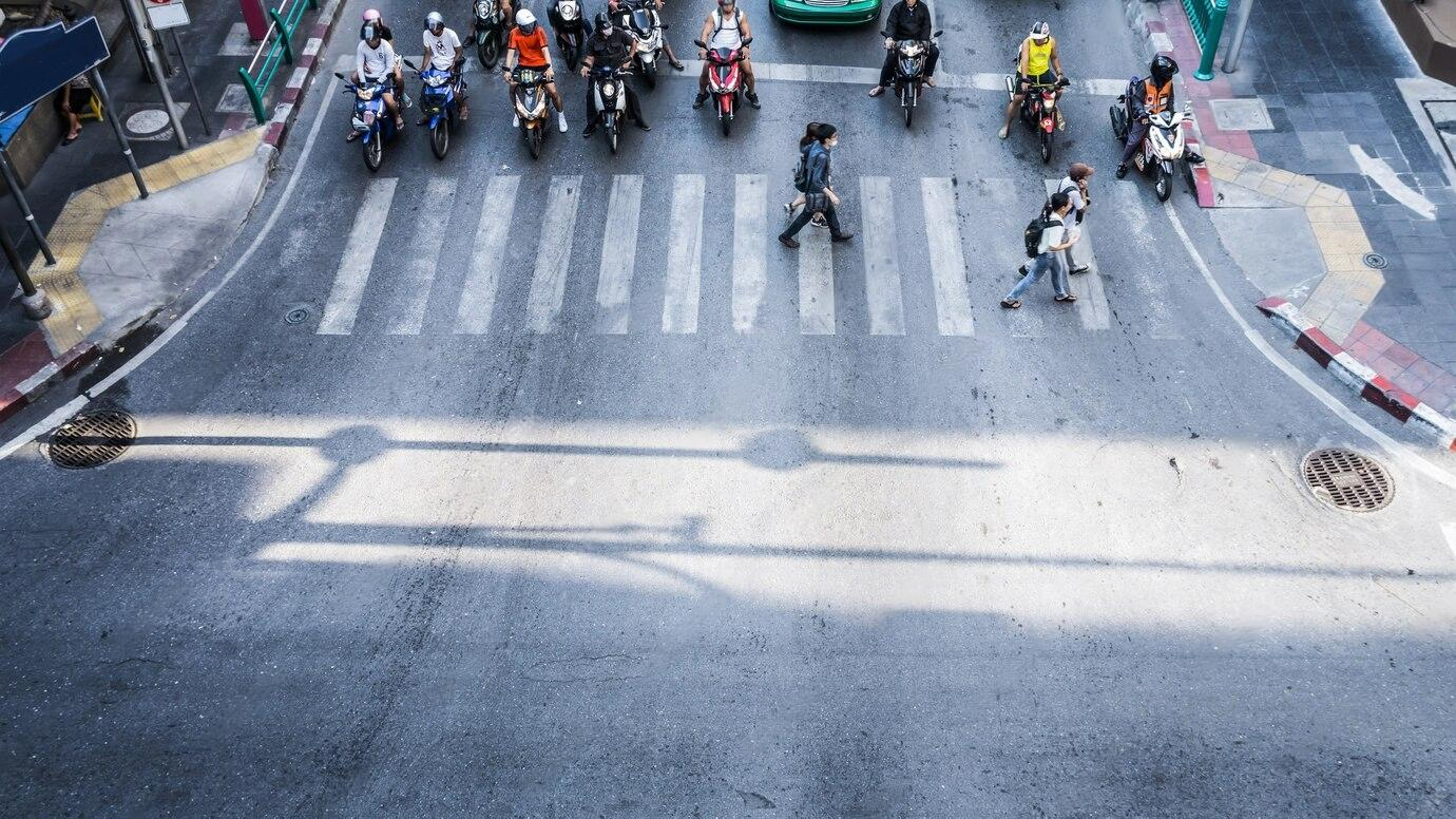 Overhead view of pedestrians and motorcycles at a city crosswalk.