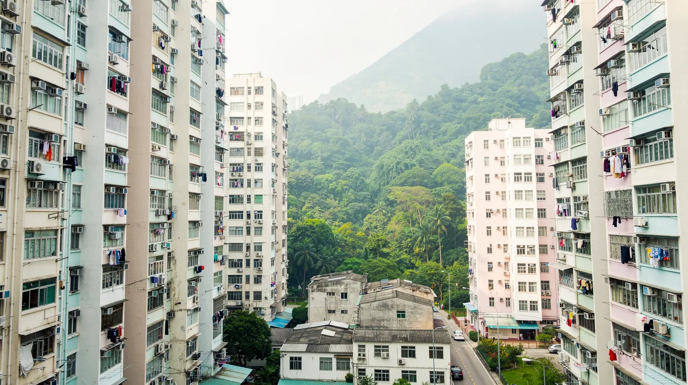 The image depicts a skyline of residential apartment buildings in Hong Kong, with lush green hills rising majestically in the background, showcasing the unique blend of urban life and natural beauty in the 香港 特別 行政區.