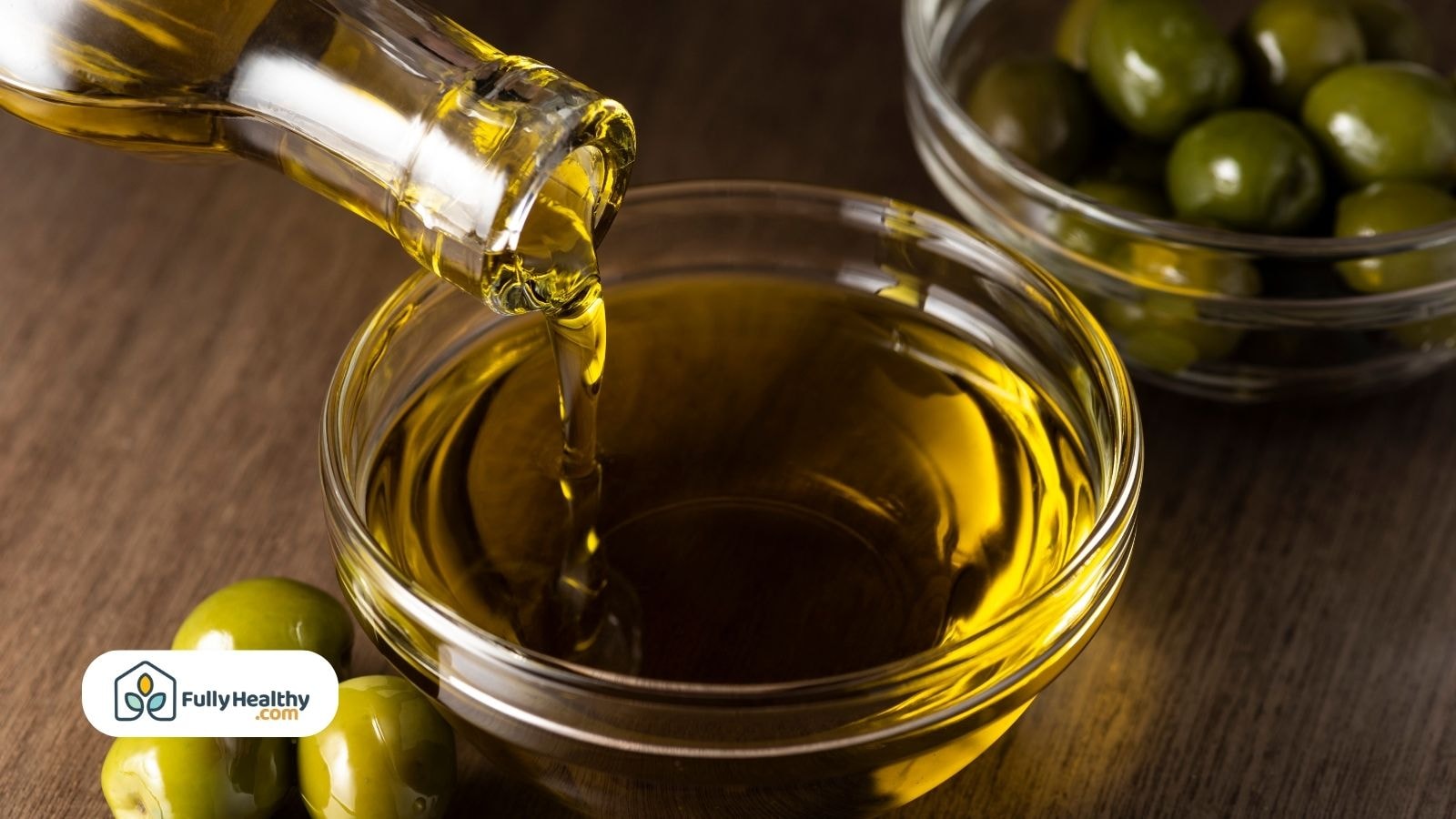Golden olive oil pouring into bowl beside green olives on table