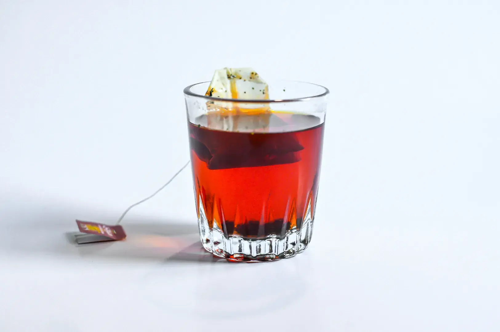 Cut-glass tumbler with a submerged tea bag steeping reddish tea.