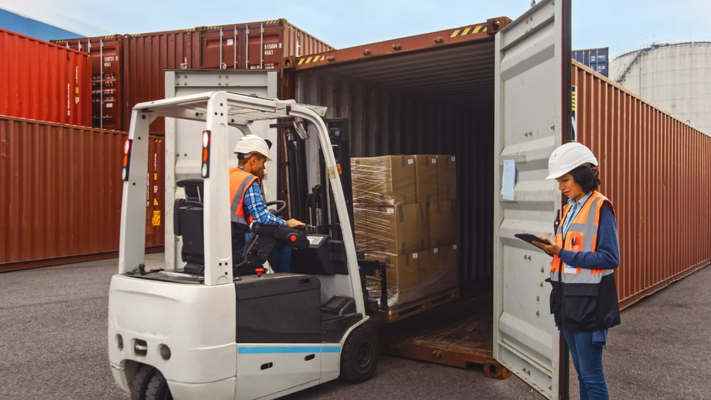 a person in a white helmet and a forklift loading a container