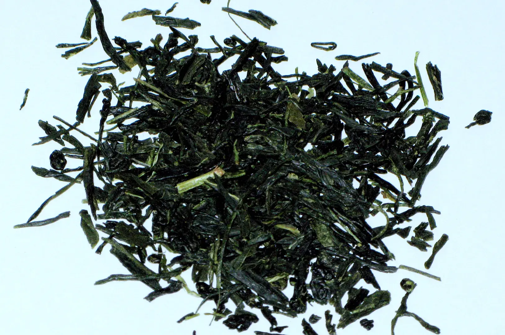 Close-up top-down view of a pile of loose, dark green needle-shaped green tea leaves scattered against a plain light background.