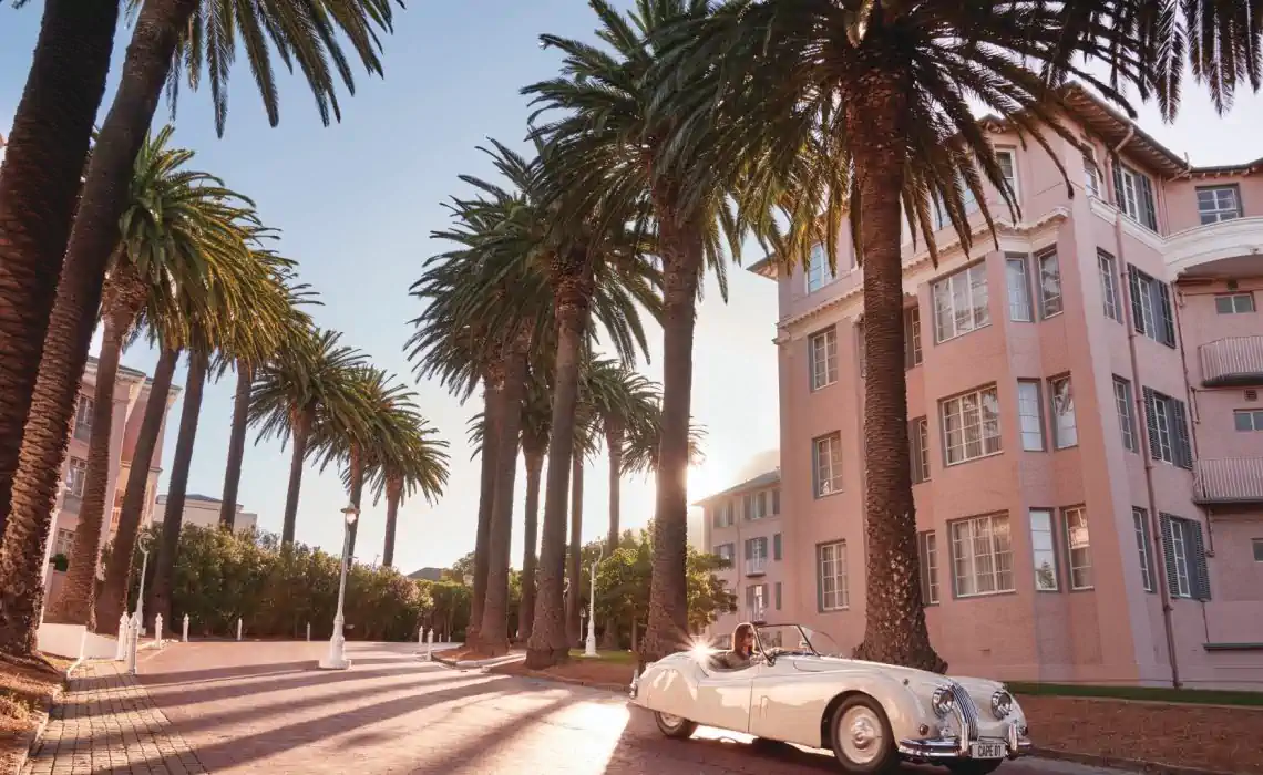 An elegant vintage car parked under swaying palm trees, with a historic building in the background. Fabulous Flowers and Gifts