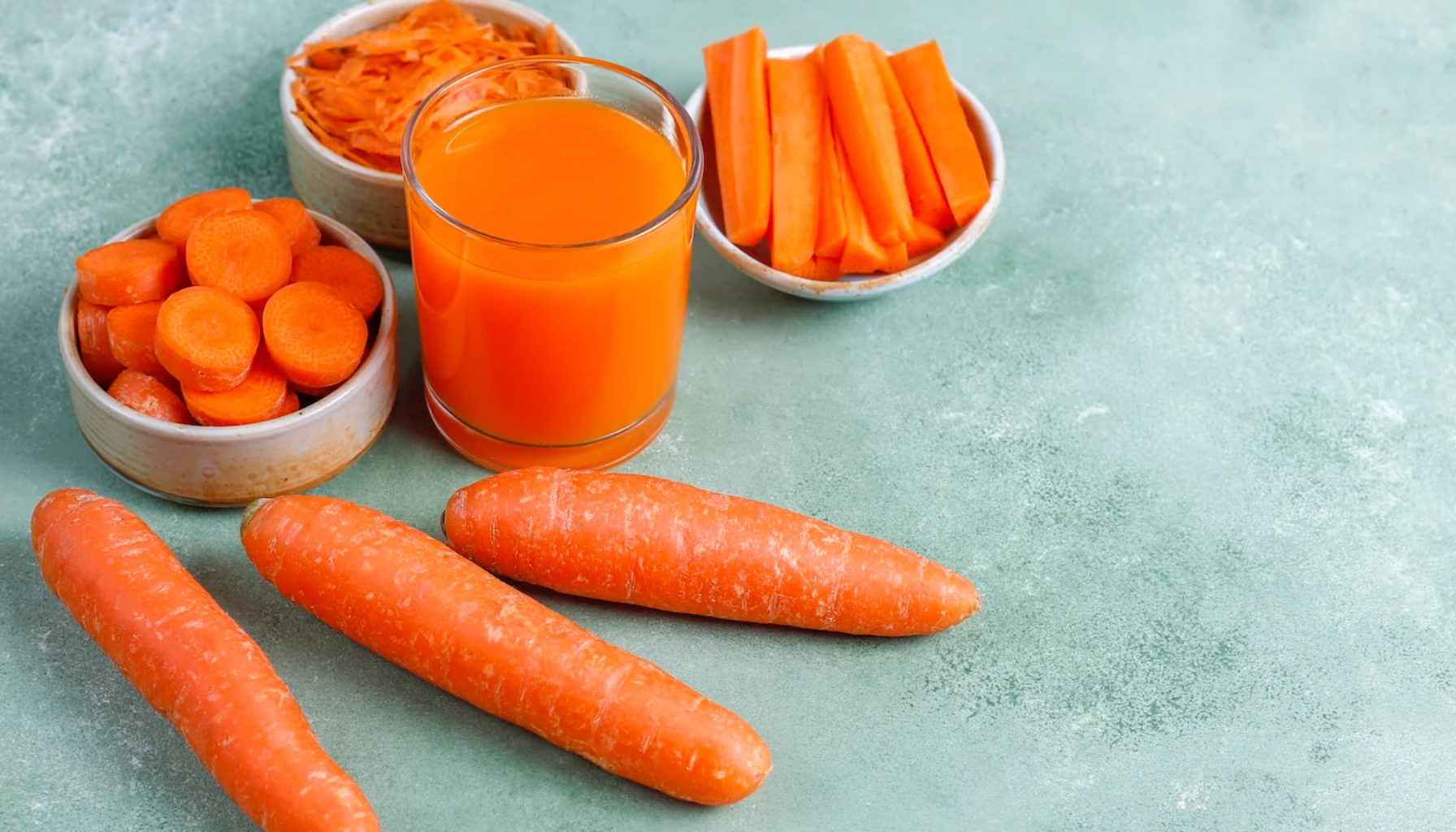 Friske gulrøtter, gulrotjuice og oppskårne biter i skåler på grønt underlag, rik på vitamin A og næringsstoffer.