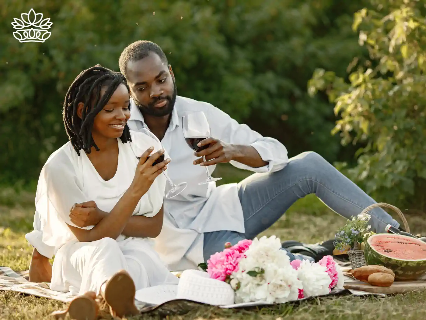 A couple enjoying a romantic outdoor picnic with wine, surrounded by lush greenery and a bouquet of vibrant pink and white flowers. Fabulous Flowers and Gifts delivered with heart. Valentine's Day Flowers.
