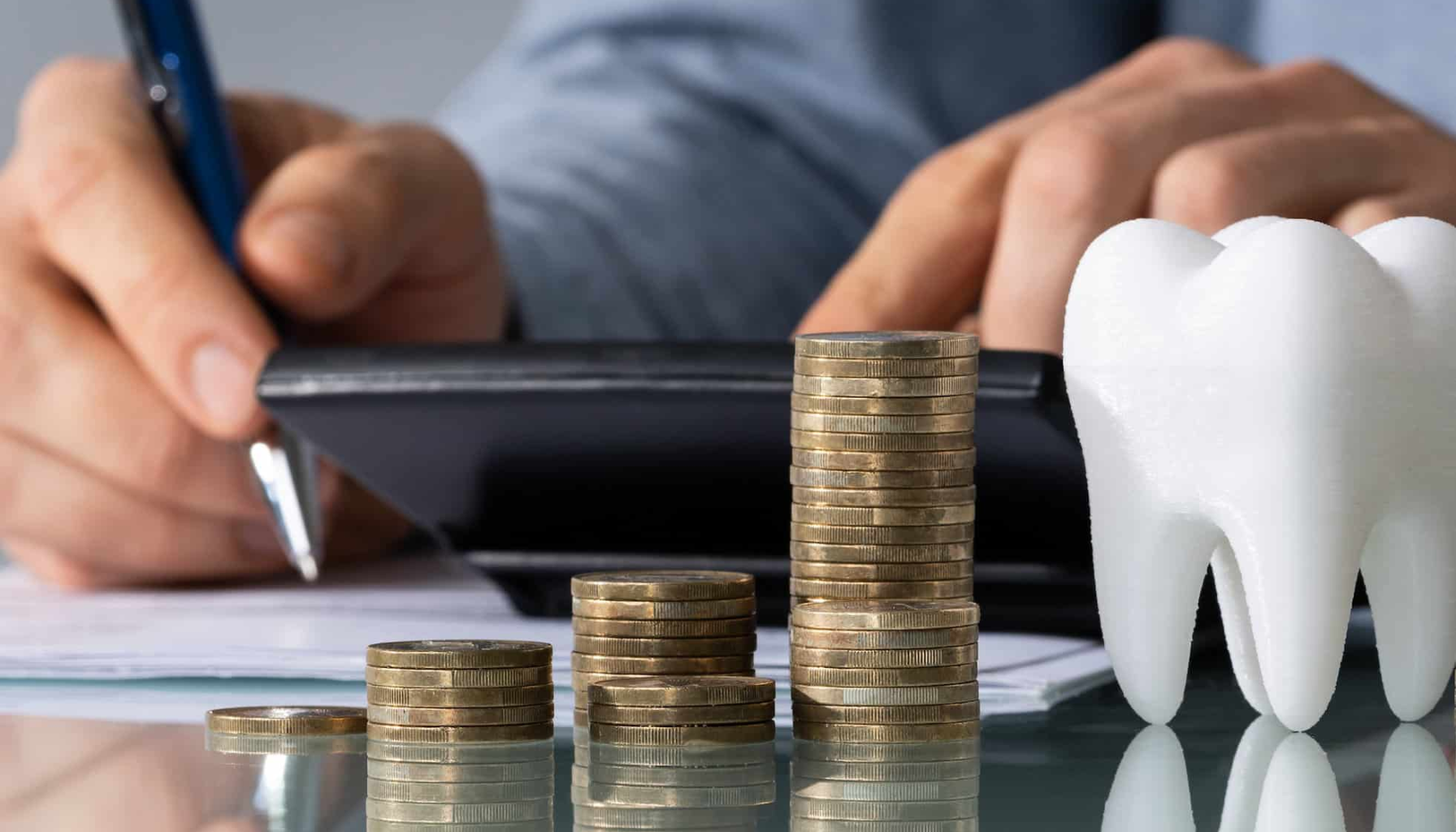 Tannhelseforsikring: En trygghet for økonomien 15 Stabler med mynter ved siden av en tannmodell, foran en person som bruker kalkulator.