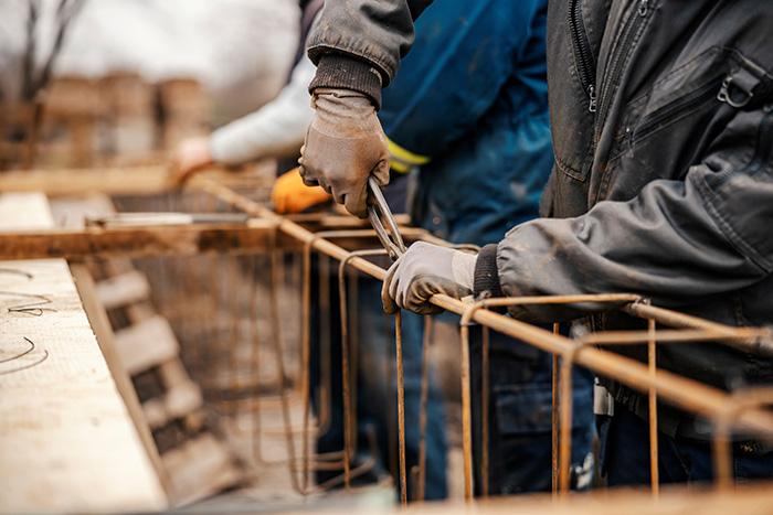 Construction workers using pliers to bend rebar on a job site illustrating workplace injury risks
