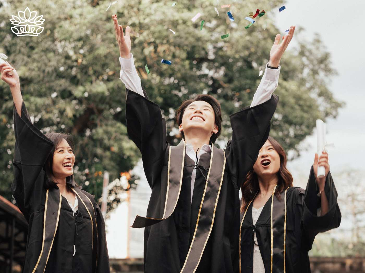 A group of three jubilant graduates, two women and one man, throwing their caps in the air during a festive graduation ceremony, celebrating their achievements with joy and excitement, courtesy of Fabulous Flowers and Gifts.