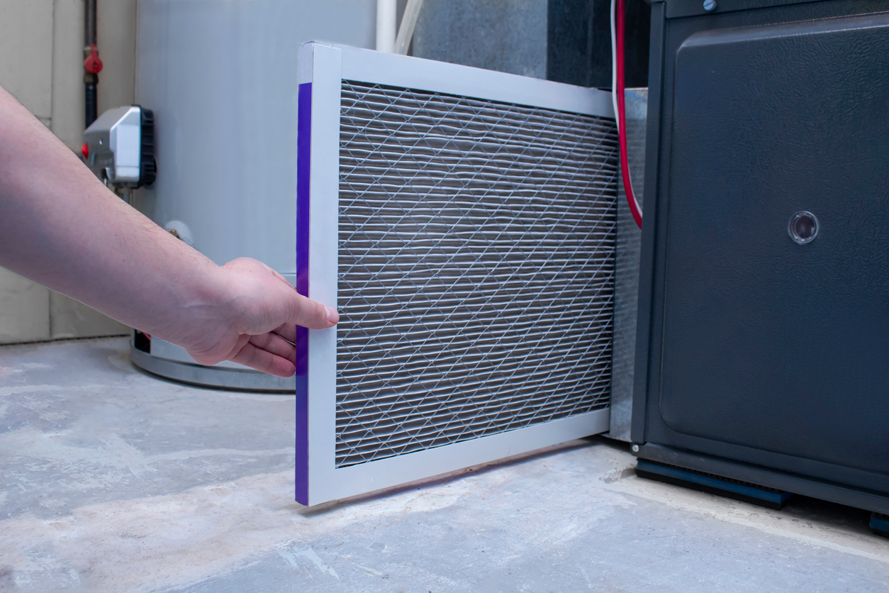 A person changing an air filter on a furnace