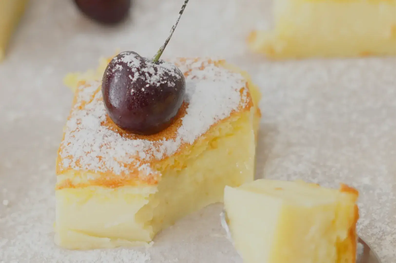 A slice of dessert topped with a cherry and dusted with powdered sugar.