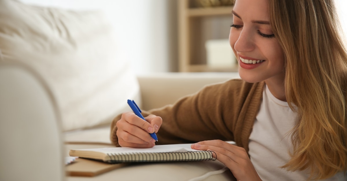 Smiling woman writing in a notebook, managing her OnlyFans business expenses list.