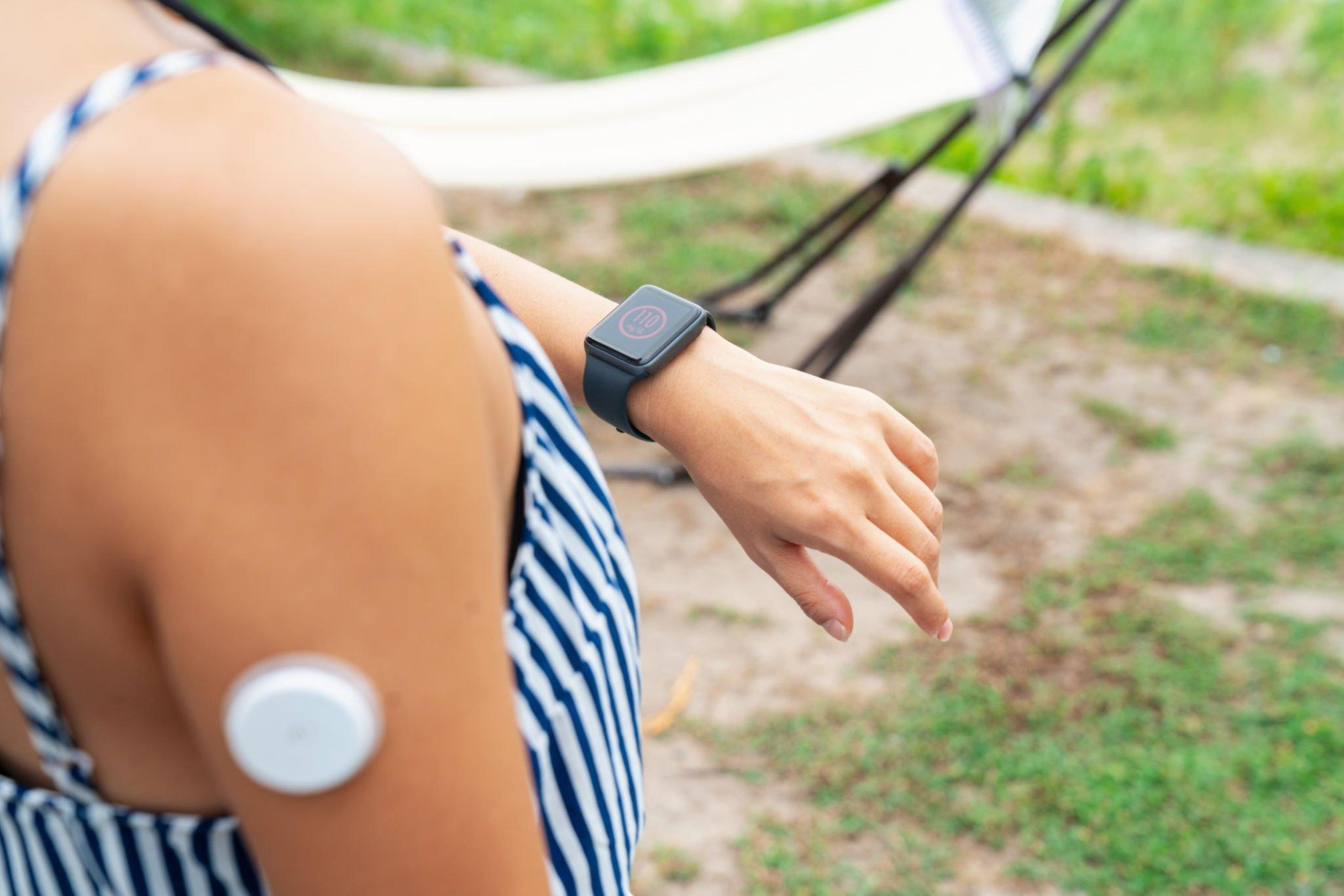 A person wearing a CGM device on their body and checking their smartwatch to remotely monitor blood sugar