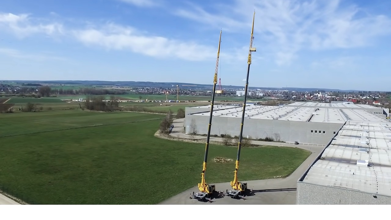 Aerial view of twin yellow cranes on industrial site near lush green field with distant urban skyline under blue sky