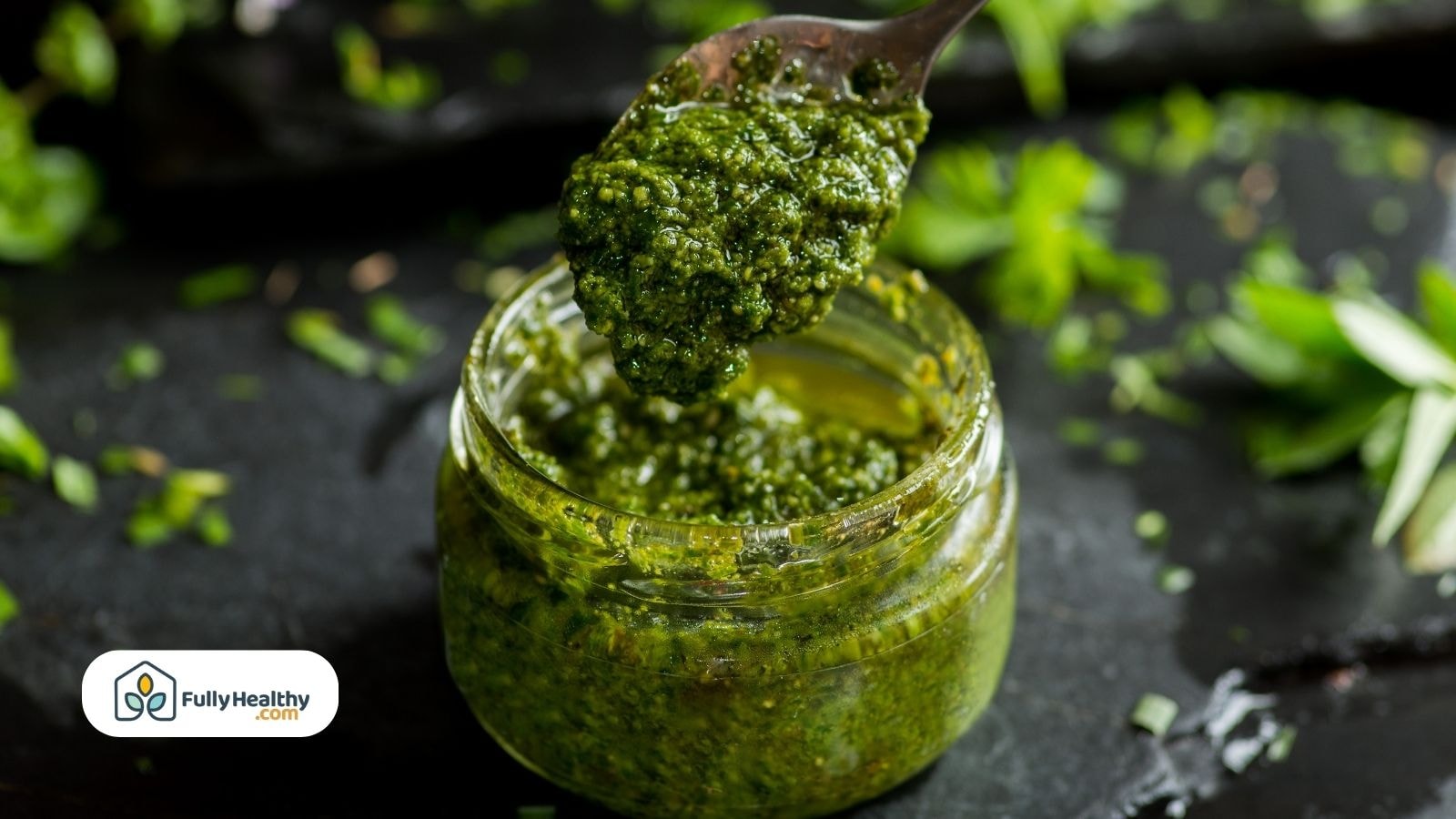 Spoonful of green pesto being lifted from a small glass jar