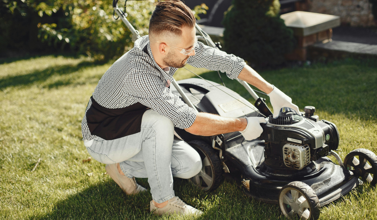 Figure checking a petrol lawn mower in the garden
