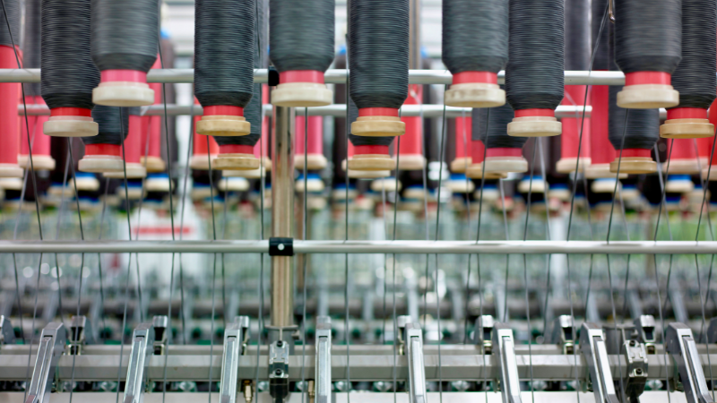 Close-up of a textile machine featuring black polyester spools, red bobbins, and visible metal mechanisms.
