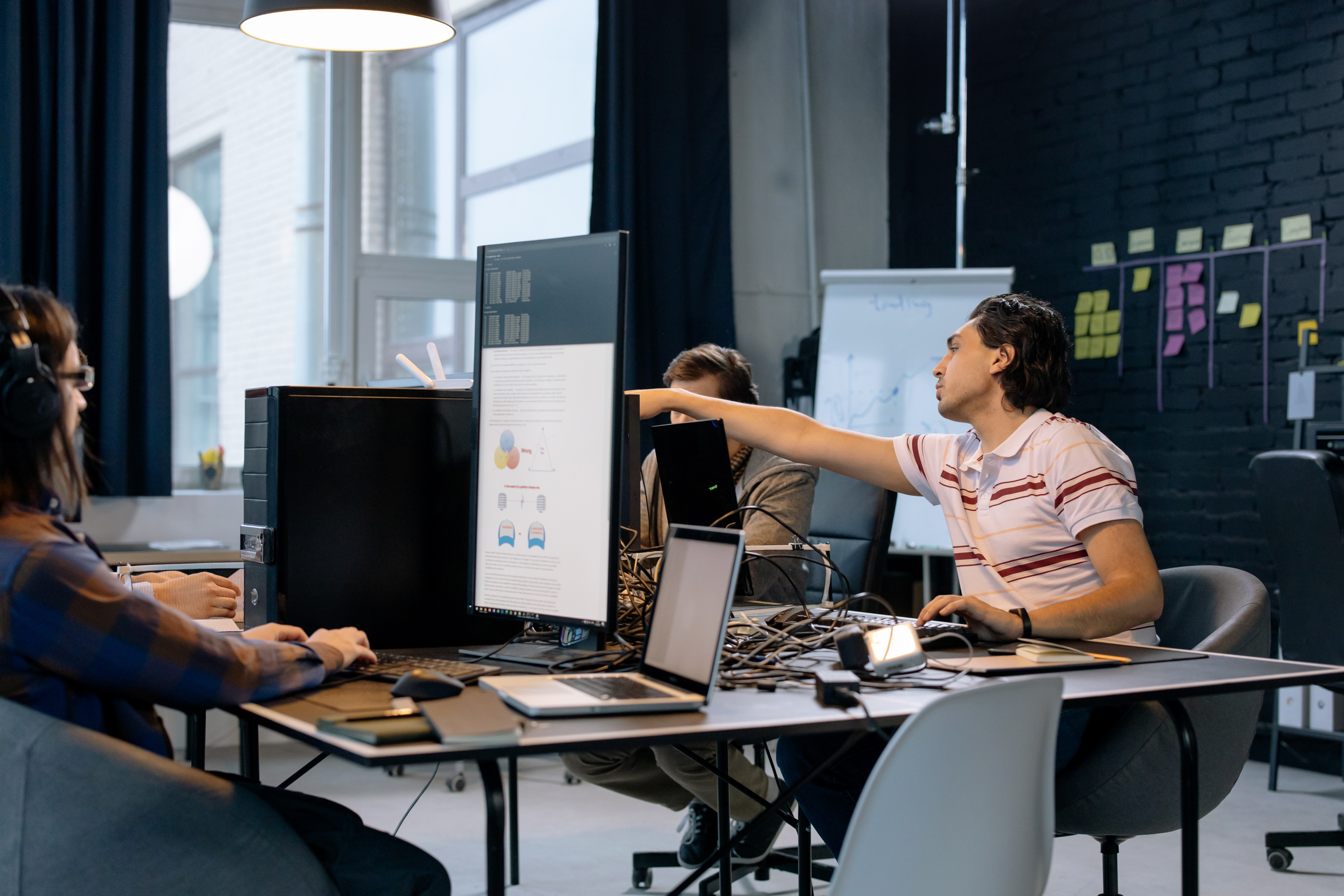 An office with 3 people sitting at a desk full of computers.