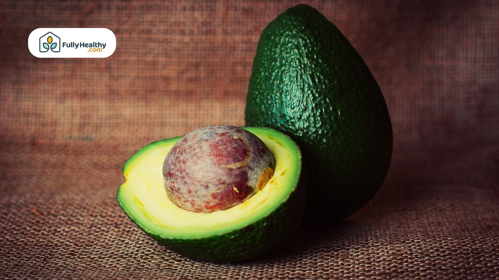 Whole avocado and halved avocado with seed on burlap background